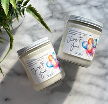 Load image into Gallery viewer, Two candles with &#39;Cheers to You!&#39; labels on a marble surface with a plant in the background.
