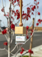 Load image into Gallery viewer, A car diffuser in the Crisp Country Coeur d&#39;Alene  scent from the Fall Candle Scent Collection hangs from the car rearview mirror.
