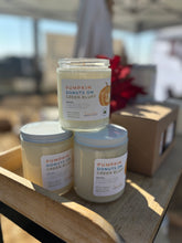 Load image into Gallery viewer, Three jars of &#39;Pumpkin Donuts on Green Bluff&#39; candles on a wooden surface with a blurred background.
