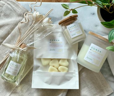 Flat lay of four Bungalow products in the Guava & Gardenia scent: 8 oz candle, mini candle, wax melts, and a wood reed diffuser.