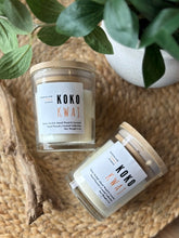 Load image into Gallery viewer, Two Koko Kwaj scented candles on a textured surface with a plant in the background
