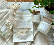Load image into Gallery viewer, Flat lay of four Bungalow products in the Lemon &amp; Basil scent: 8 oz candle, mini candle, wax melts, and a wood reed diffuser.
