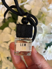 Load image into Gallery viewer, Bungalow car diffuser in the Lemon scent held in front of white flowers.
