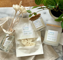 Load image into Gallery viewer, Flat lay of four Bungalow products in the Linen &amp; Leaf scent: 8 oz candle, mini candle, wax melts, and a wood reed diffuser.
