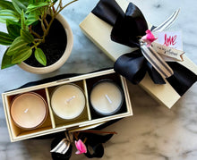 Load image into Gallery viewer, A trio of candles in different colors placed in a cream linen box with black satin ribbon, alongside a potted plant and a tag that reads 'LOVE'. The box is adorned with a signature striped cotton ribbon.
