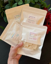 Load image into Gallery viewer, 4 white packages of heart shaped wax melts being held together in front of a green plant 
