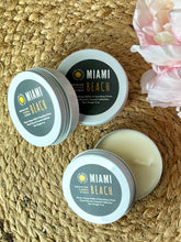 Load image into Gallery viewer, Three travel candle tins with a black label in the Miami Beach scent on a woven surface with flowers.
