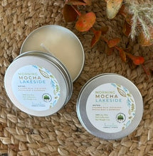 Load image into Gallery viewer, Two silver metal tin travel candles in the scent, &quot;Morning Mocha Lakeside&quot; arranged open and closed on a woven surface with decorative fall leaves in the background.

