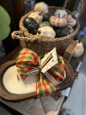 Oval Dough Bowl candle tied with a fall ribbon, sitting on table with mini pumpkins in a basket as decor in the background.