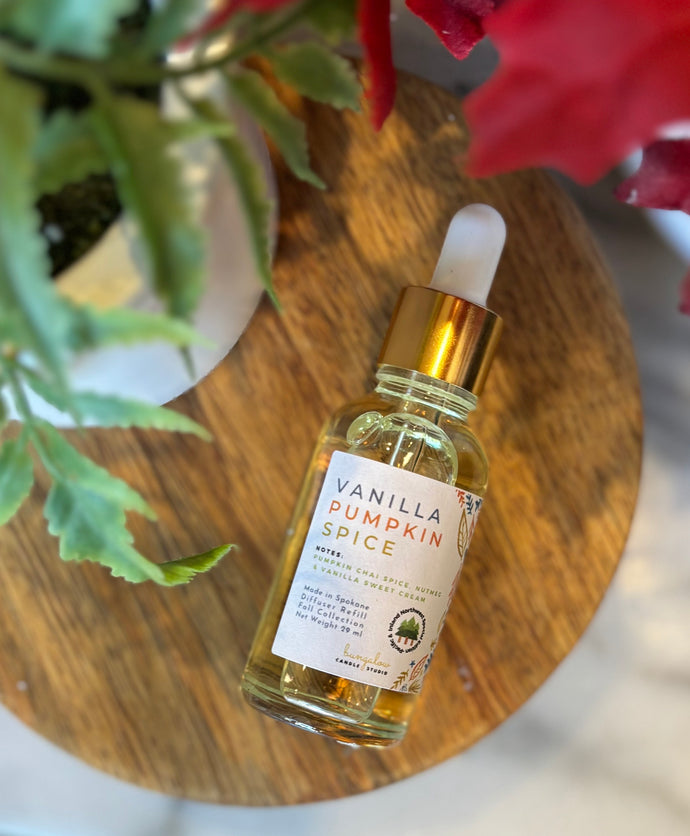 Bottle with dropper lid of 'Vanilla Pumpkin Spice' scented fragrance oil on a wooden surface with flowers in the background