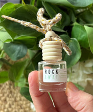Load image into Gallery viewer, Car diffuser in a small apothecary bottle in the 'Rock Away' scent held in a hand in front of a green leafy background.
