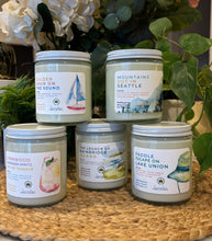 Load image into Gallery viewer, Group of 5 Bungalow Seattle Collection soy wax candles that are 8oz size in glass jars with white tin lids stacked on a woven mat with greenery in the background.
