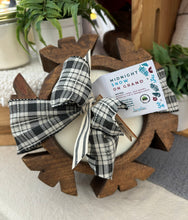 Load image into Gallery viewer, A hand-carved wood dough bowl candle in the shape of a snowflake with a checkered black and cream ribbon sitting on a table.
