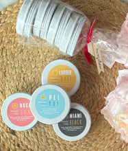 Load image into Gallery viewer, Travel candles stacked in front of a packaged bundle on a woven mat.
