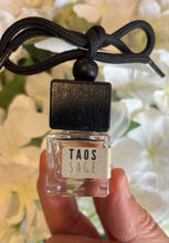 Load image into Gallery viewer, Bungalow car diffuser in the Taos Sage scent held in front of white flowers.
