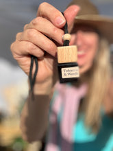 Load image into Gallery viewer, Sue, owner of Bungalow Candle Studio holding the Cedar &amp; Forest scent from the Cascade Collection in a car diffuser.
