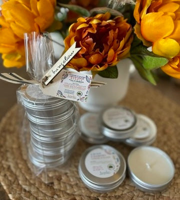 Travel Tin Candles in a bundle and stacked individually with labels indicating various fall scents, arranged on a woven surface with decorative pumpkins and leaves in the background.