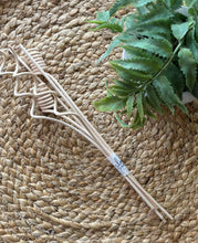 Load image into Gallery viewer, A bundle of twisty-shaped wood reeds for diffusers displayed diagonally on a woven straw placemat next to a green artificial fern plant.
