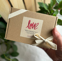 Load image into Gallery viewer, Hand holding a brown Kraft box tied with ribbon with a tag showing it is for the LOVE scent.
