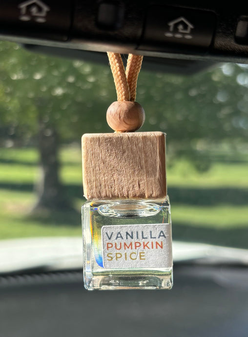 A car diffuser in the Vanilla Pumpkin Spice scent from the Fall Candle Scent Collection hangs from the car rearview mirror.