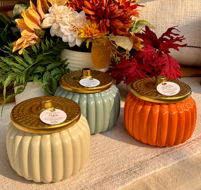 Three decorative jars with gold lids on a surface with flowers in the background