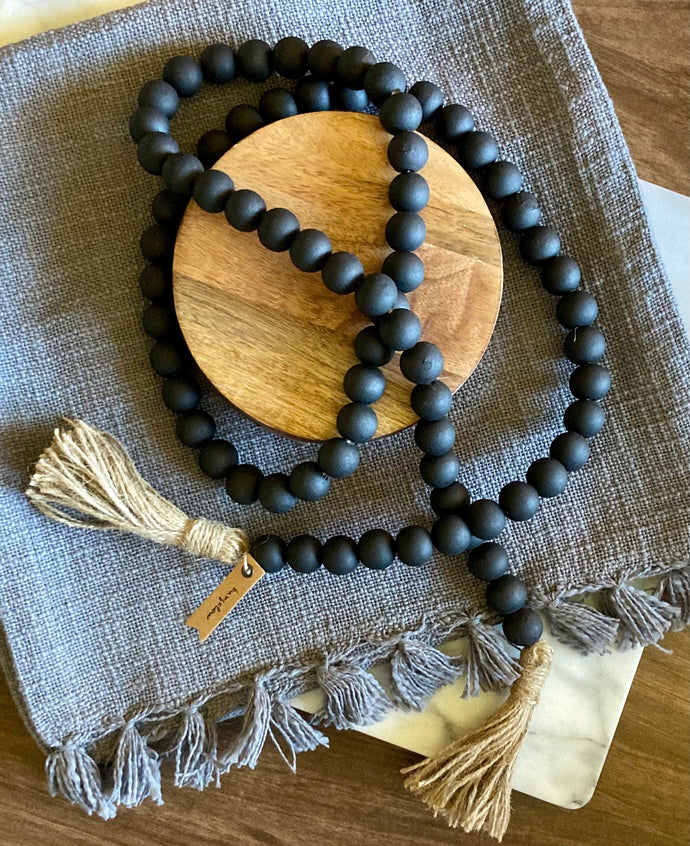 A string of Mango Wood Contentment Beads hand-painted in matte black and draped on a table as home decor.