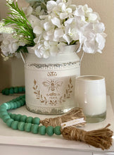 Load image into Gallery viewer, A string of sage green contentment beads made from Mango Wood placed on table next to vase and candle as home decor.
