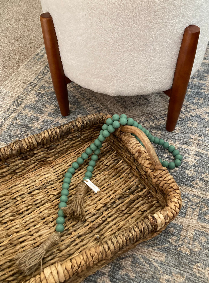 A string of sage green contentment beads made from Mango Wood draped over basket as home decor.