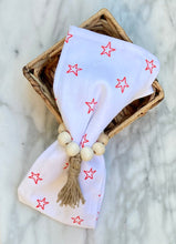Load image into Gallery viewer, Natural beige colored mango wood bead napkin holder, holding white napkin with red stars propped on a basket on a marble table
