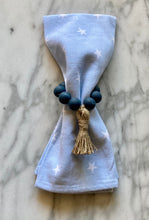 Load image into Gallery viewer, Navy colored mango wood bead napkin holder, holding blue napkin with white stars on a marble table
