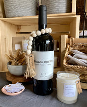 Load image into Gallery viewer, Wine bottle displayed with natural mango wood bead garland around it like a necklace.
